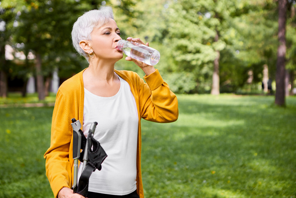 пожилая женщина пьет воду после скандинавской ходьбы